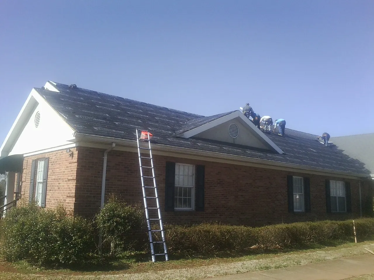 Crew tearing shingles off a brick ranch roof with a ladder set — Metal Roof Repair work by our crew in North Conway