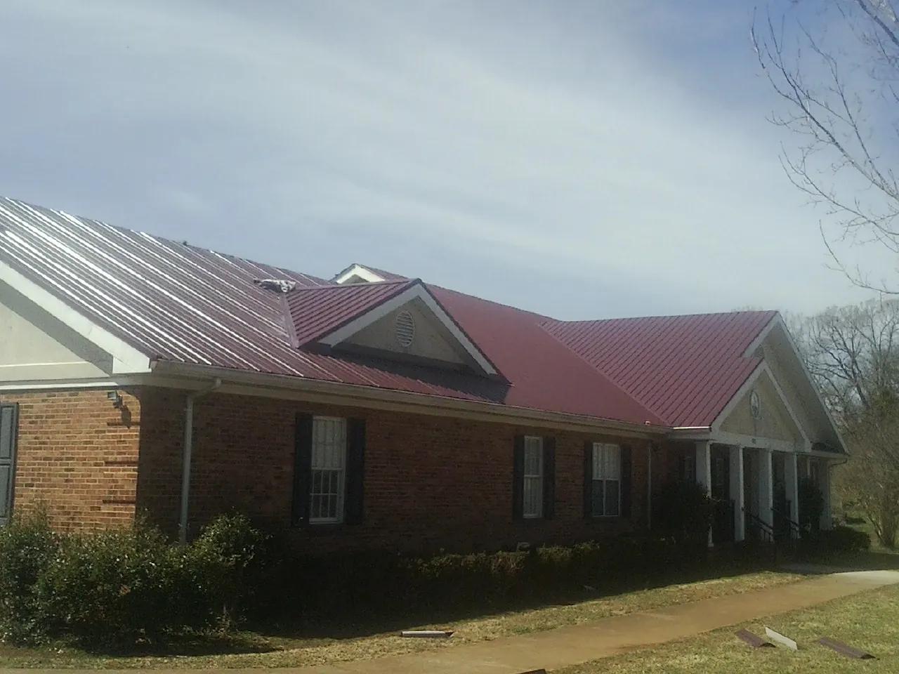 Red metal roof with gabled entries on a long brick building, from a Hail Damage Roof Repair job in North Conway