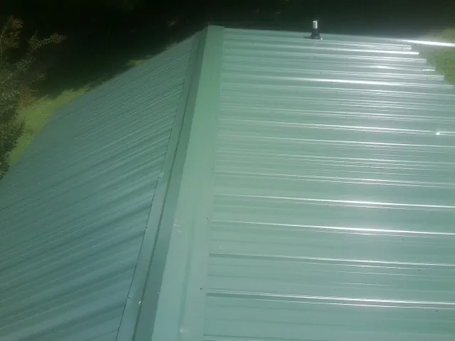 New green metal panels meeting at the ridge of a roof — Flat Roof Repair work by our crew in North Conway