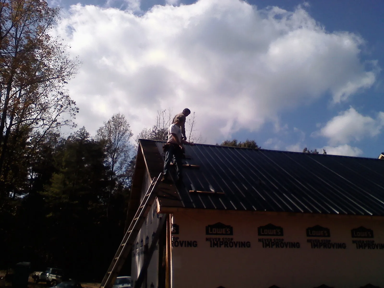 Roofer fastening dark metal panels high against a cloudy sky, from a Roof Inspection job in North Conway