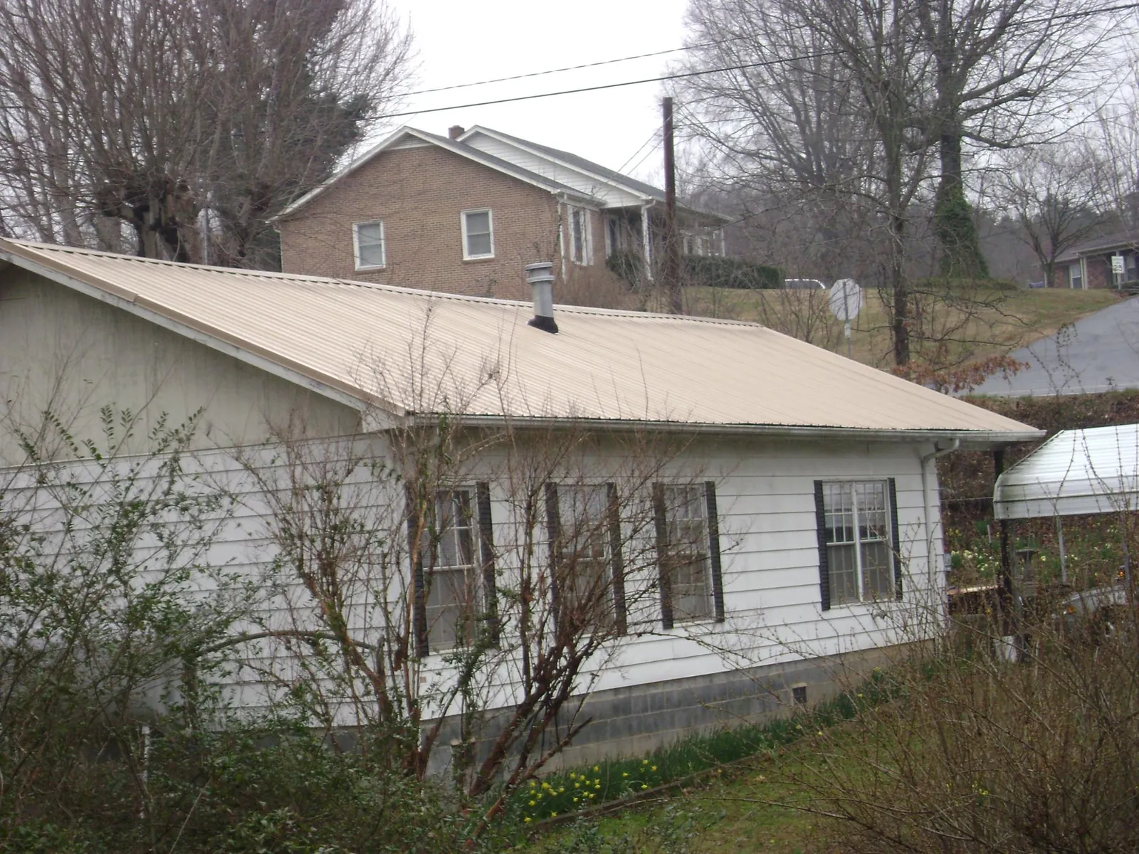 Tan metal roof on a white sided house set into a hillside — Commercial Roofing by Roofing Brothers in North Conway