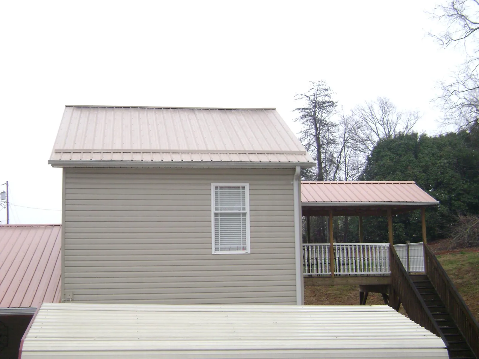 Tan metal roofs on a two story addition and attached porch, from a Roof Replacement job in North Conway